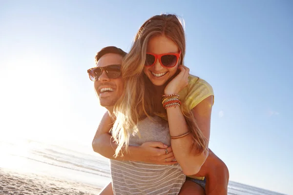 太陽の下で愛と笑い ハンサムな若い男がガールフレンドにビーチでピギーバックを与え — ストック写真
