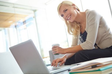 İyi bir iş anlaşması yapıyoruz. Ofiste dizüstü bilgisayarı üzerinde çalışırken elinde kahve tutan bir şirket kadını.