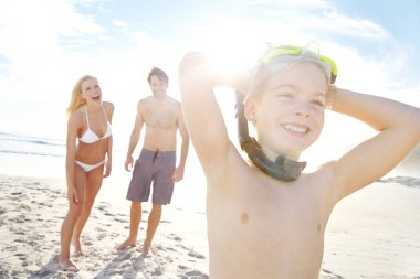 Güneş eğlenceyi ortaya çıkarıyor. Gözlük takan küçük mutlu bir çocuk plajda ailesiyle bir gün geçiriyor.