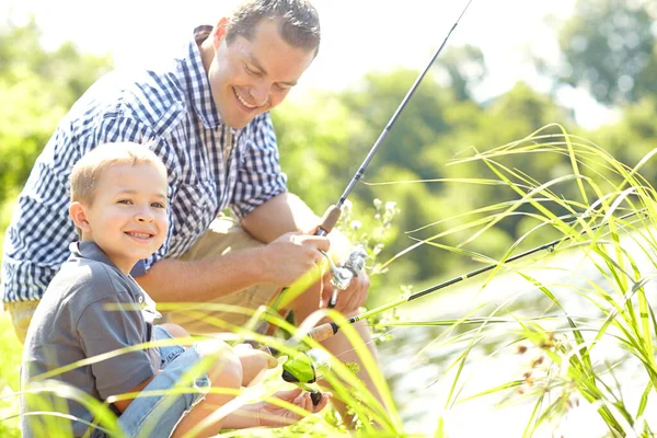 stock image Enjoying a new experience with dad. Cute young boy sitting beside his dad and learning how to fish