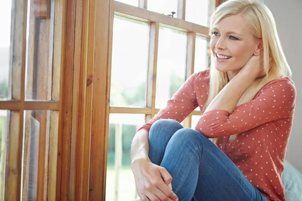 一个美丽的女人笑着坐在房子里的窗边 快乐迷人的金发女人在家里冷 快乐的女性在一个享受周末和我的时间的公寓里放松 — 图库照片