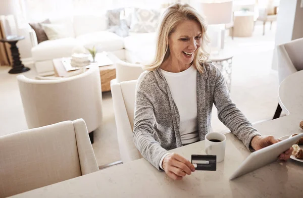 stock image The home shopping experience. a mature woman using a credit card and digital tablet while relaxing at home