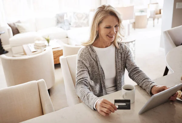 stock image Spending some well earned money. a mature woman using a credit card and digital tablet while relaxing at home