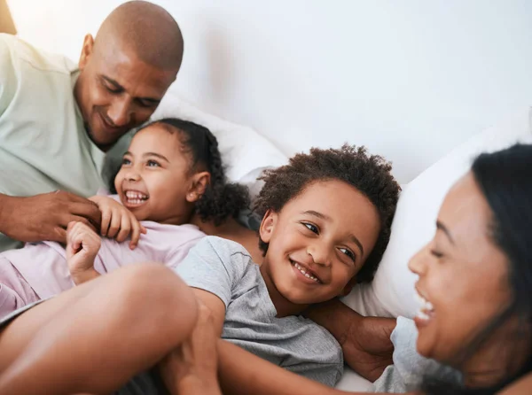 stock image Happy family, relax and playing in the morning on bed with smile for free time, weekend or fun holiday at home. Mother, father and children relaxing and laughing together for playful joy in bedroom.