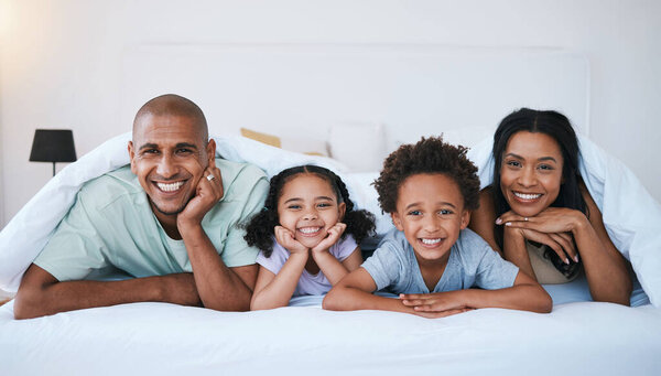 Portrait, family and smile in bedroom blanket in home, bonding and relaxing or lying. Bed, happiness and children with mother and father enjoying quality time together, having fun and care in house