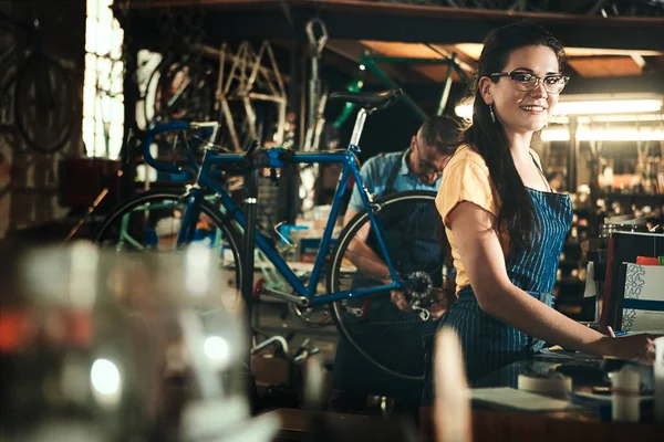 Small business owners aka the dream makers. Portrait of a young woman working in a bicycle repair shop with her coworker in the background