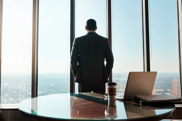 stock image Focused on steering his career in the right direction. Rearview shot of a young businessman looking out the window in an office
