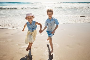 Plaj onların yaz oyun alanı. Kumsalda el ele koşan iki sevimli genç çocuk.