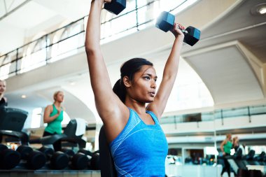 Kaldırın. Spor salonunda dambıllarla çalışan çekici bir genç kadın.