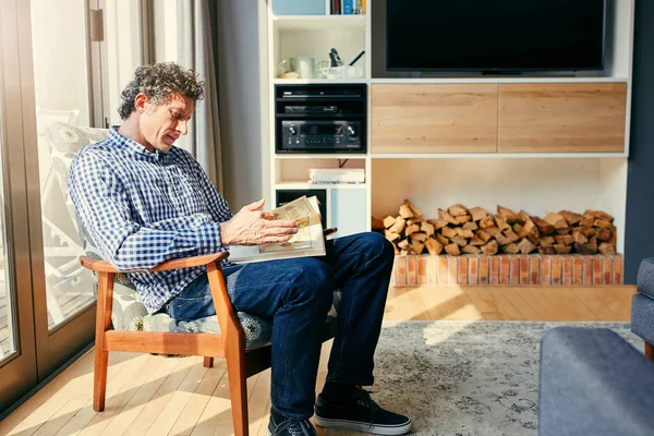 stock image Reading in the sunlight. a focused middle aged man seated on a chair while reading a book at home during the day