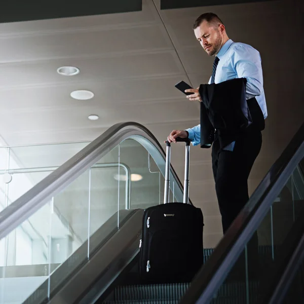 Airplane mode - on. a businessman using a mobile phone while traveling down an escalator in an airport