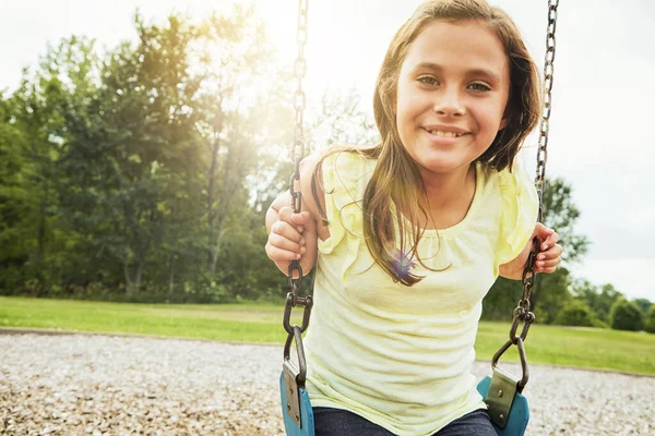 子供の頃の喜び 公園でスイングで遊んでいる若い女の子の肖像画 — ストック写真
