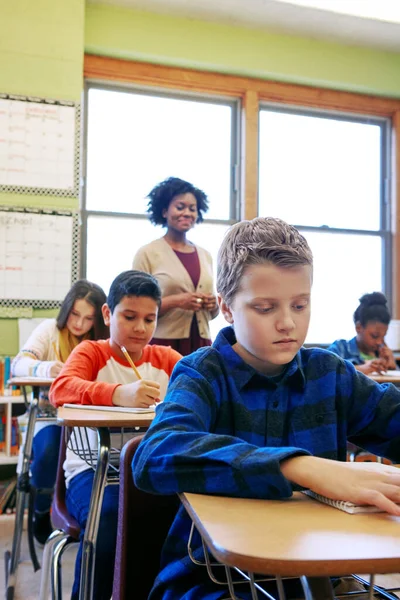 Assessment is a critical step in the learning process. a young boy sitting in class with his teacher and classmates blurred in the background