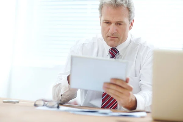 デジタルドキュメントの編集 事務所の机に座っている間にタブレットを持っている成熟したビジネスマン — ストック写真