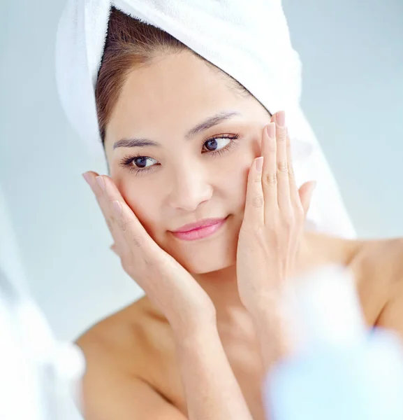 stock image Fresh-faced beauty. An attactive young Asian woman applying moisturizer with a towel on her head