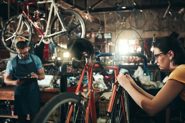 让旧的自行车死而复生在自行车修理店工作的年轻妇女 其背景是她的同事 — 图库照片