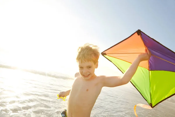 Nothing beats flying a kite at the beach. a little boy running while holding a kite on a beach