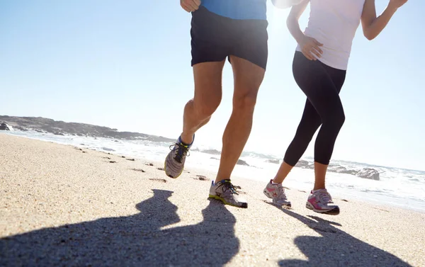 stock image Taking fitness outdoors. a young couple jogging together on the beach