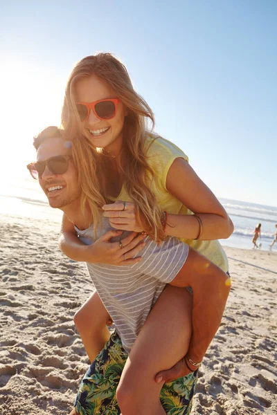 日没に乗って ハンサムな若い男がガールフレンドにビーチでピギーバックを与え — ストック写真