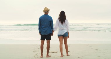 Mükemmel bir sahil randevusu. Gün boyunca plajda yan yana yürüyen sevgi dolu genç bir çiftin tam boy dikiz görüntüsü.