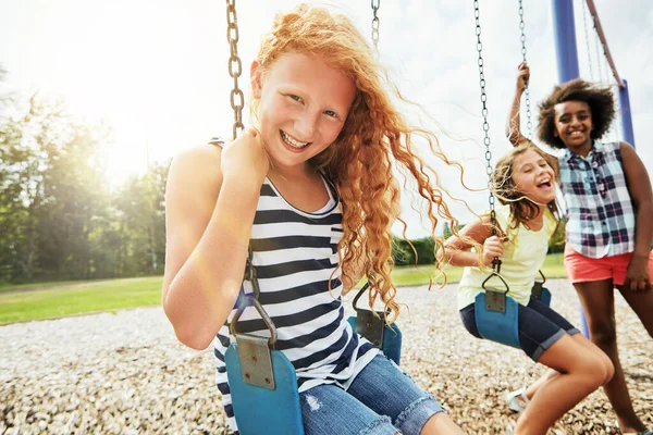 太陽の下での楽しみのトンの時間 彼女の友人と公園でスイングで遊んでいる若い女の子の肖像画 — ストック写真
