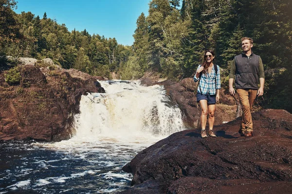 Stock image Go where youve never been. a young couple walking next to a rocky river and waterfall