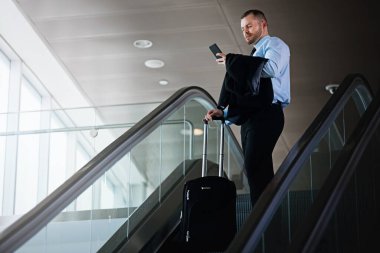 Zeki bir iş gezgini. Havaalanında yürüyen merdivenden inerken cep telefonu kullanan bir işadamı.