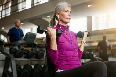 Vücudunu yeniden keşfetmek için asla çok yaşlı değilsindir. Spor salonunda ağırlık çalışan son sınıf bir kadının portresi.