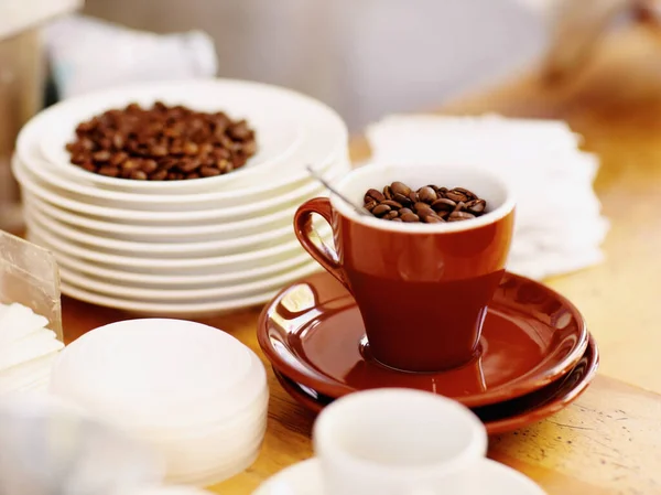 Cup, roasted coffee beans and cafe industry or shop with quality product for marketing or catering. Texture, abstract or background with brown grain as drink, espresso or caffeine ingredient on table.