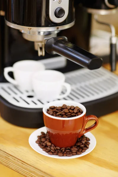 Coffee beans, cups and machine on table in cafe for cappuccino, latte or hot drink. Restaurant, electrical appliance and caffeine mugs for making or brewing espresso in retail shop or small business