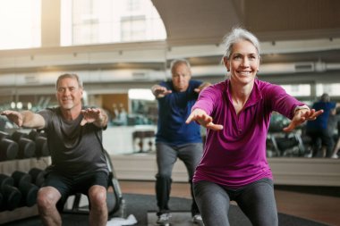 Şimdi çömel. Son sınıf bir kadın ve erkek grubu spor salonunda birlikte çalışıyor.