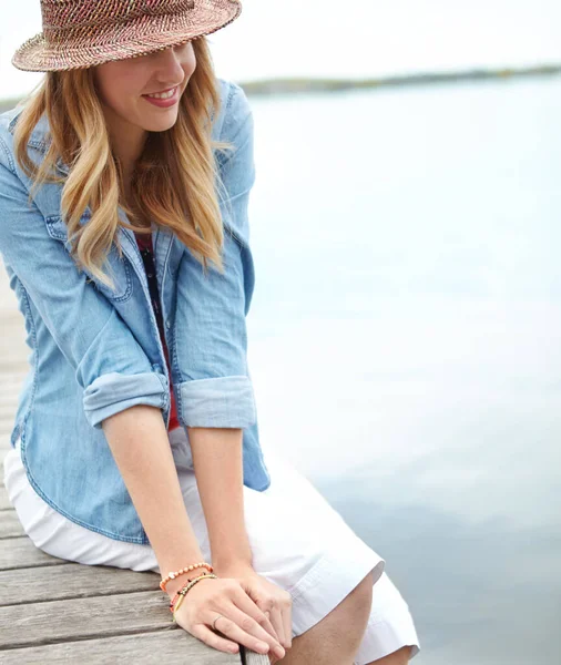 stock image Enjoying a relaxing holiday. A happy young woman sitting on a jetty next to a lake