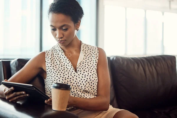 Always keep in touch with the business world. a young businesswoman drinking coffee and using a digital tablet while sitting on a couch in her office