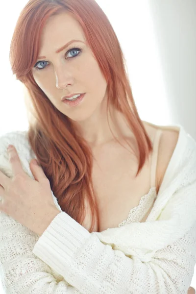 stock image Portrait of one beautiful young redhead woman relaxing home. Confident female feeling flirty, sensual and sexy while posing seductively in a warm jersey exposing her shoulder and and bra.