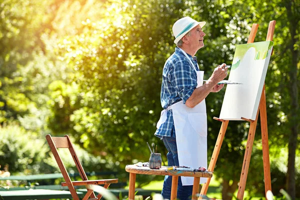 Hell be painting until the sun goes down. a senior man painting in the park