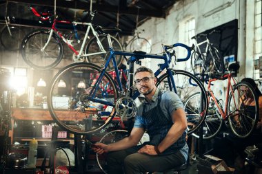 Size en kaliteli hizmeti sunmak için sertifikalı. Arka planda iş arkadaşıyla bisiklet tamirhanesinde çalışan olgun bir adamın portresi.
