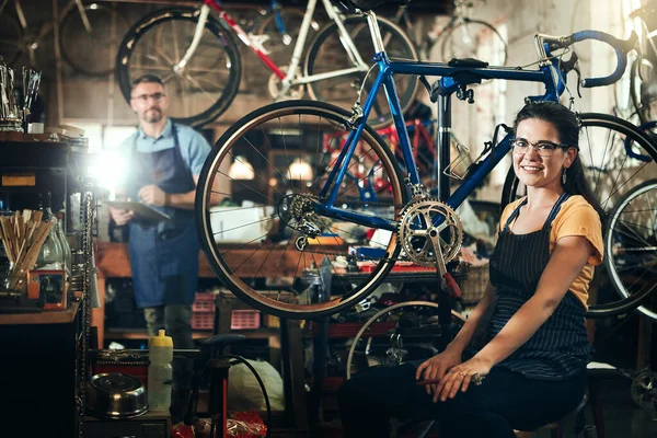 我们都很喜欢自行车 一个年轻女子和她的同事在自行车修理店工作的肖像 — 图库照片