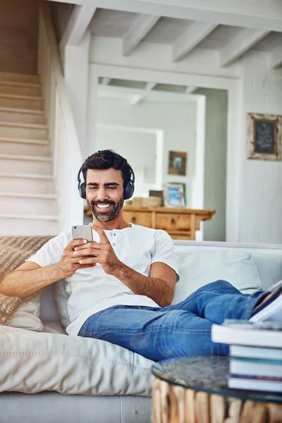 美妙的曲调让人放松 用电话和耳机在沙发上休息的男人 — 图库照片