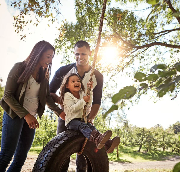 家族としてのつながり 幸せな母親と父親が娘たちをタイヤスイングに押し込み — ストック写真