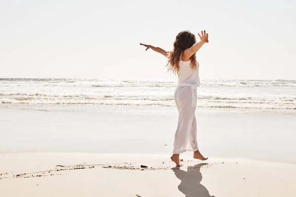 She has such a free spirit. Rearview shot of a young woman standing with her arms outstretched at the beach