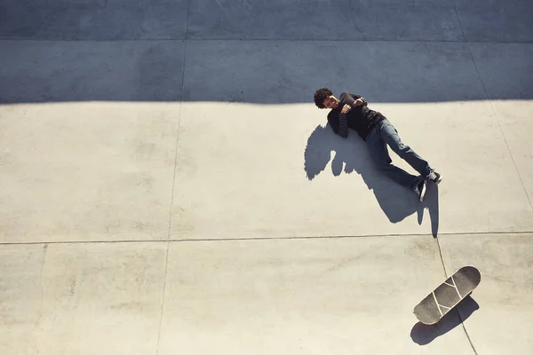 坠落是游戏的一部分 在一个滑板公园 一个年轻人躺在自己滑板旁边的地板上拍了一张高角的照片 — 图库照片