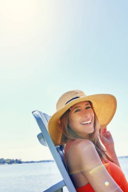Dışarıda tek başıma yaşayacağım. Güneşin altında gölün yanındaki sandalyede otururken şapka takan neşeli genç bir kadının portresi.