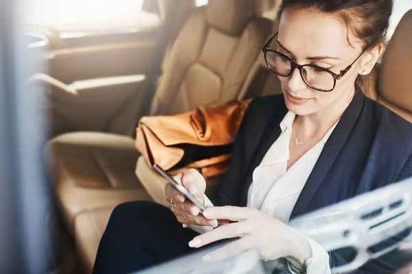 stock image Going to try and get as much work done as possible. a confident young businesswoman seated in a car as a passenger while texting on her phone on her way to work