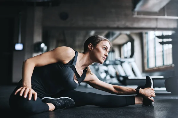 stock image Shes proof that discipline and determination pay off. an attractive young woman stretching during her workout in a gym