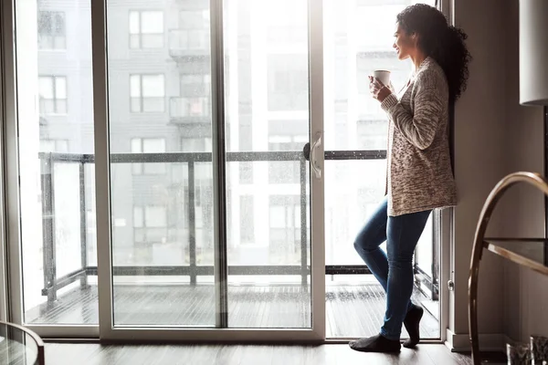 stock image Life is so much better when youre relaxing. a cheerful young woman drinking coffee while looking through a window inside at home during the day