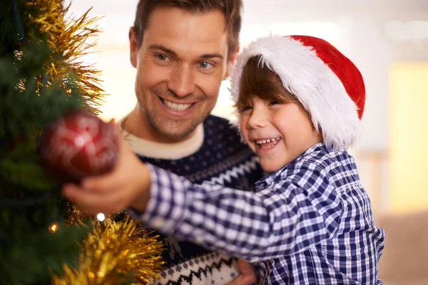 お祝いの気分に入る 父親と一緒にクリスマスツリーを飾る若い男の子 ストックフォト
