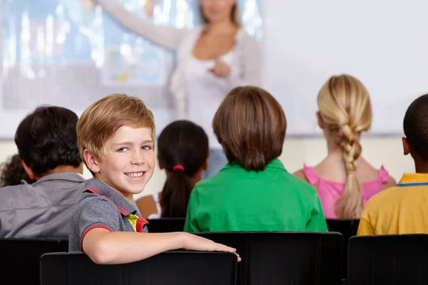 学校总是有趣的 一个微笑的男孩和他的其他学生坐在教室里的画像 — 图库照片