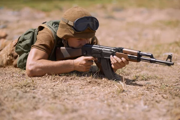 Stalking the enemy. A young soldier aiming with his rifle while lying on the ground