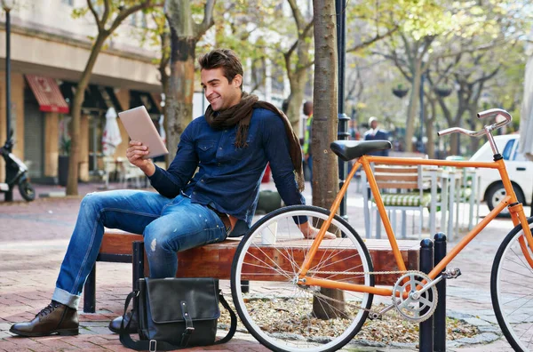 stock image Catching up on some news while taking a break. a man using his tablet while taking a break in the city with his bicycle beside him