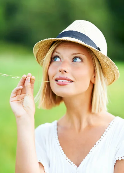 屋外でリラックス 帽子をかぶっている間に微笑む魅力的な若い女性と小麦の茎を噛む — ストック写真